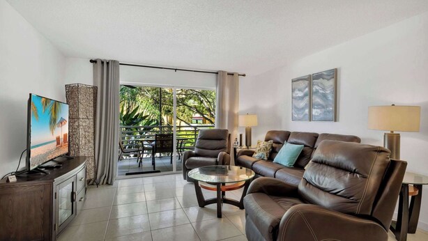 Una sala de estar con sofá, sillón, televisor y una mesa de vidrio.