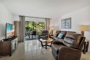 A living room with a sofa, armchair, TV, and a glass table. - Le Frontenac 204 STR-03583 (Sunny Isles Beach)