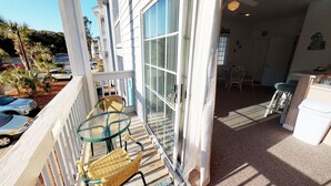 Un balcon doté d’une porte vitrée, de chaises en osier, d’une petite table et offrant une vue sur les voitures garées et les arbres.