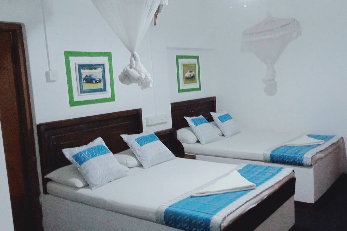 Een hotelkamer met twee enkele bedden, een houten nachtkastje, een garderobe en twee ingelijste foto’s aan de muur.