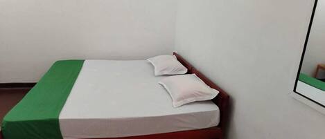 Una habitación pequeña con cama individual, colcha verde y blanca, dos almohadas y cabecera de madera.