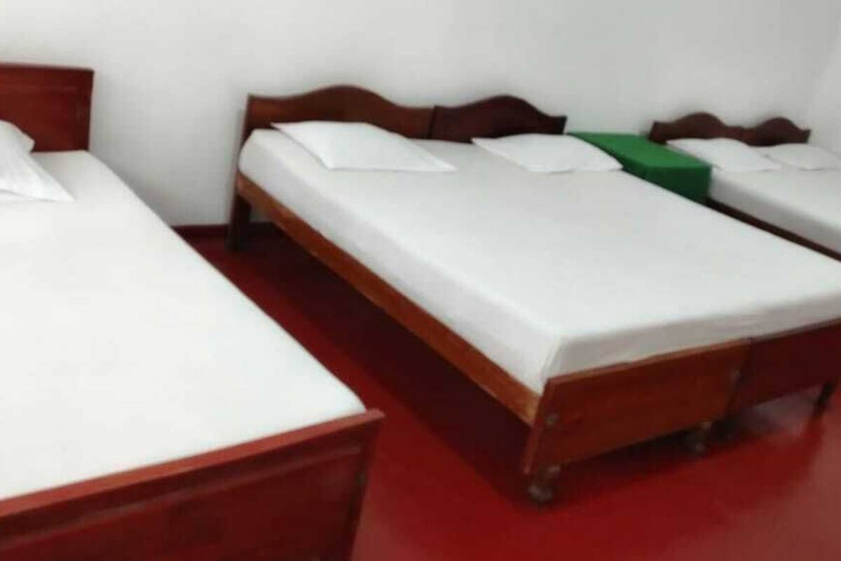 Een kamer met drie eenpersoonsbedden, elk met een houten hoofdbord en witte beddengoed.