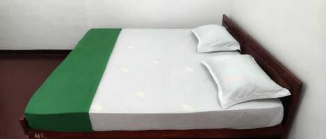 Una cama con colcha verde y blanca, dos almohadas y cabecera de madera.