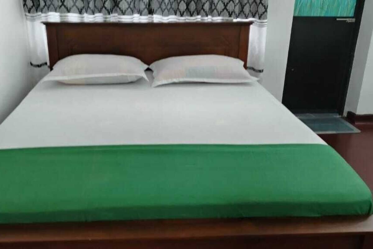 Een bed met een groene deken en witte kussens, een houten hoofdbord en een zwarte deur op de achtergrond.