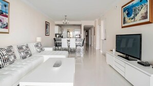 A modern living room with a white sofa, a flat-screen TV, and artwork on the walls. - Le Marina Bay 1006 STR-01435 (Sunny Isles Beach)
