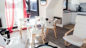 Een compacte leefruimte met een eethoek, kitchenette en uitzicht door een groot raam.