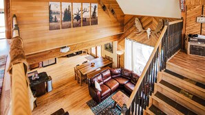 Amplio espacio tipo loft con techo de madera, un sofá grande de cuero, zona de comedor y una escalera.
