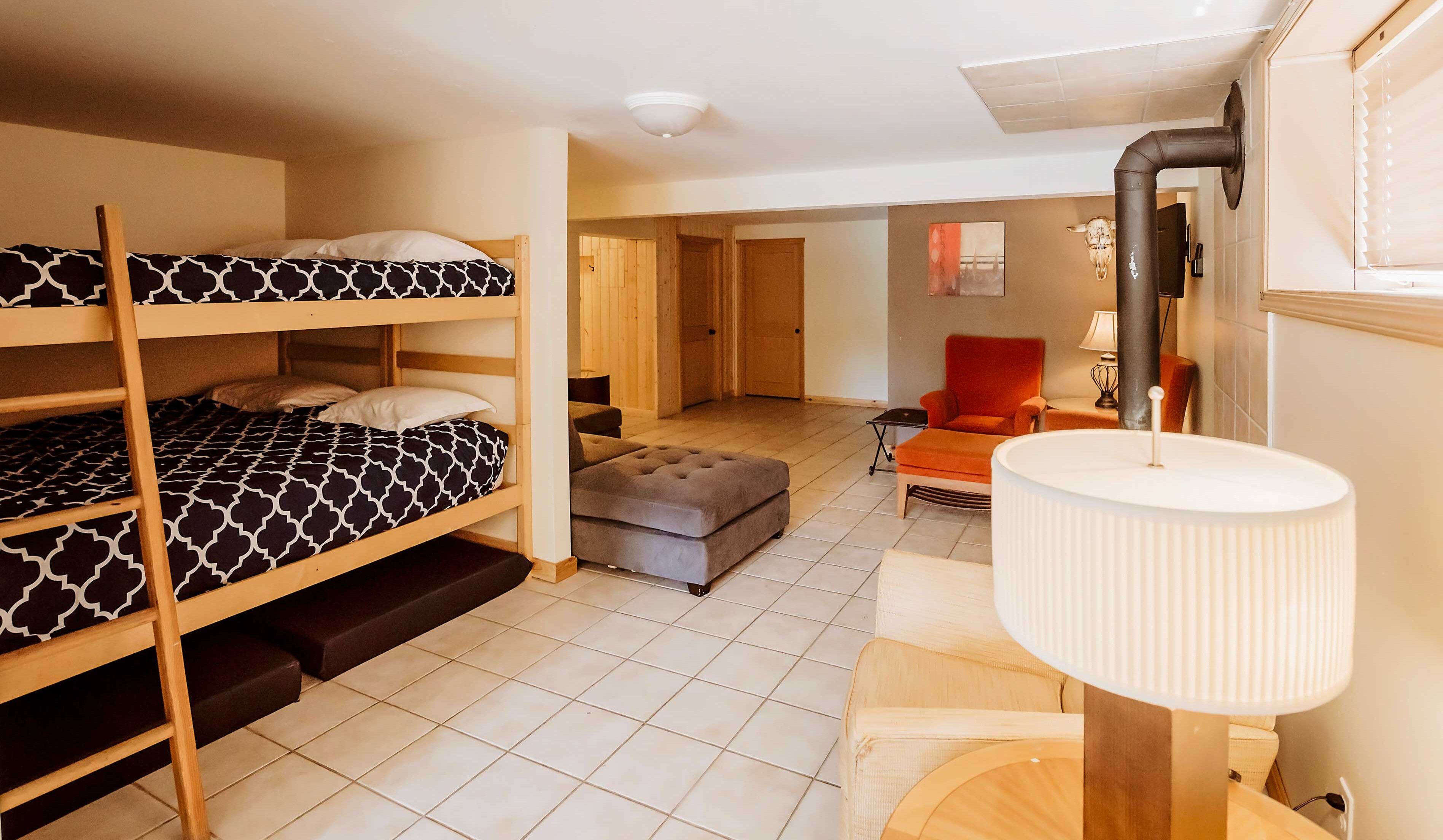 Quarto em dormitório com beliches, um pequeno sofá, uma cadeira e um abajur.