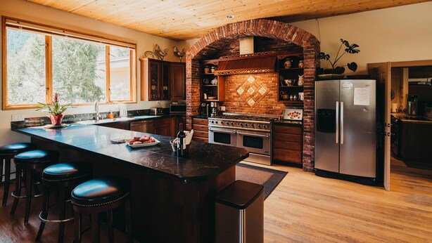 Una cocina con una isla grande, taburetes de bar, un refrigerador y un protector contra salpicaduras de ladrillo.