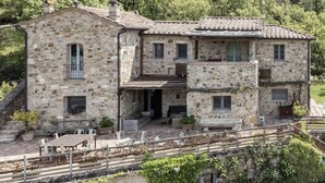 Ein Steinhaus mit Balkon, Außenbereich zum Sitzen und Blick auf einen bewaldeten Hügel.