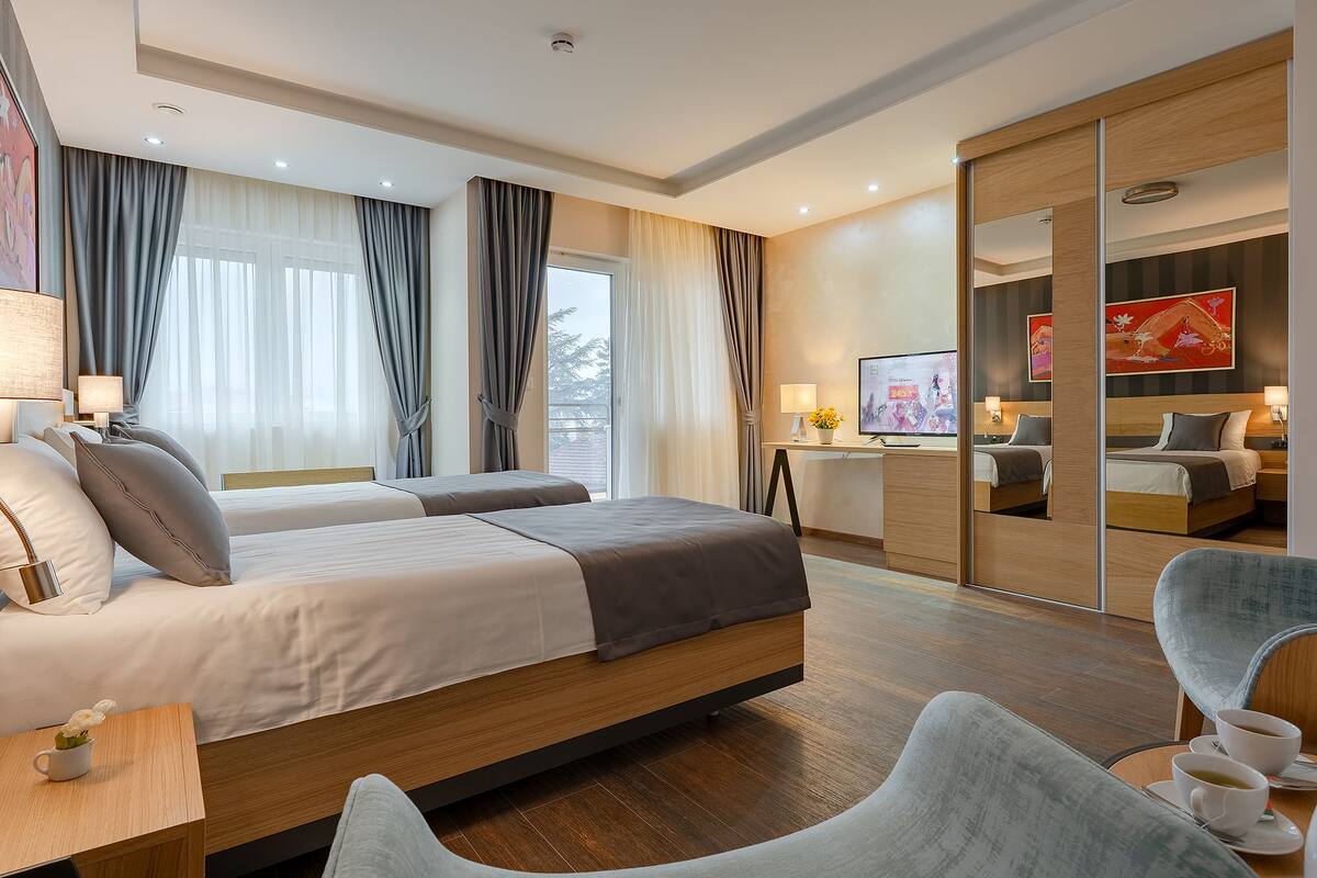 A modern hotel room with two beds, a desk, and a TV.