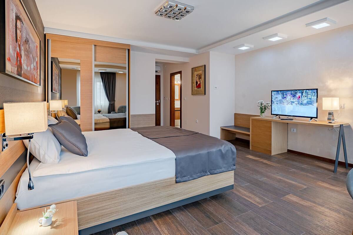 A modern hotel room with a large bed, a desk, a television, and a mirror.