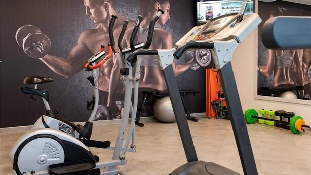 Un gimnasio con equipo cardiovascular, un espejo grande y accesorios para levantamiento de pesas.