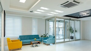 Un área de espera moderna con un sofá azul, un sillón amarillo y una mesa de centro con un jarrón de flores.