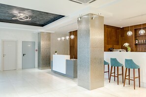 Un área de recepción moderna con un mostrador, tres taburetes de bar, lámparas colgantes y una pared decorativa de madera.
