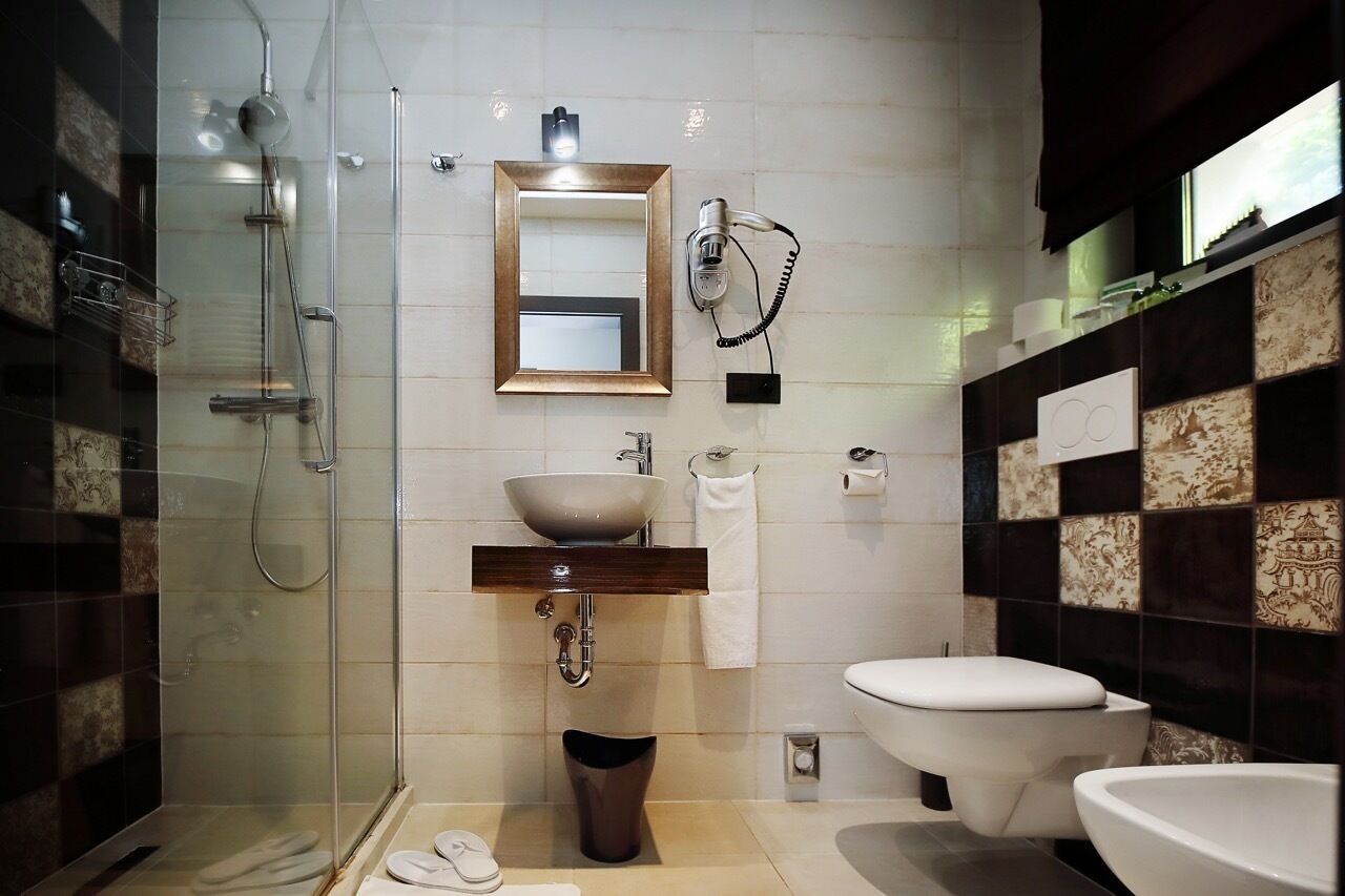 A modern bathroom with a glass-enclosed shower, a wooden vanity, a white sink, a toilet, and a bidet.