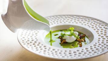 A white bowl with a green sauce being poured into it, placed on a perforated white plate.