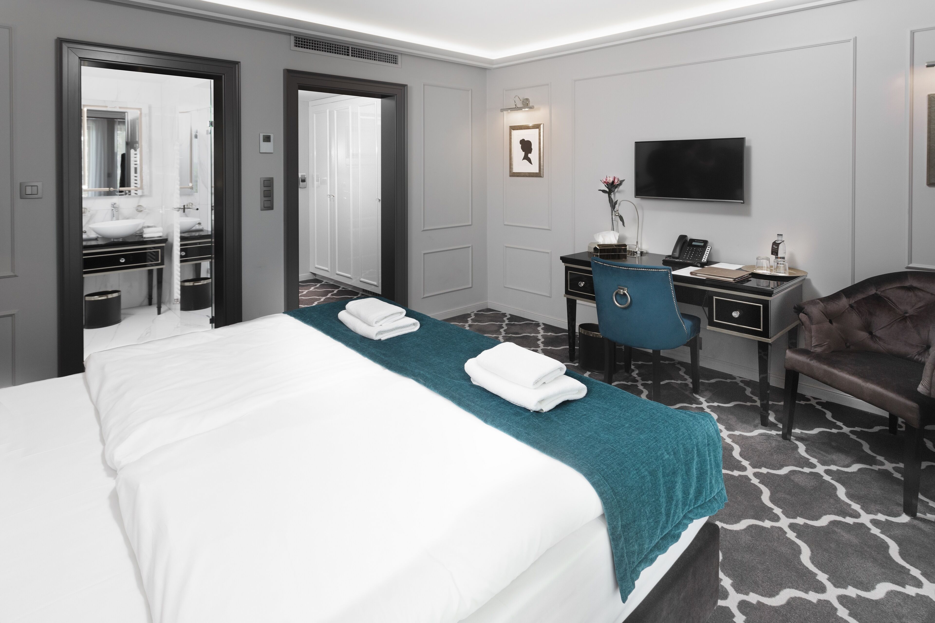 A hotel room with a large bed, a desk with a chair, a TV, and a bathroom visible through an open door.