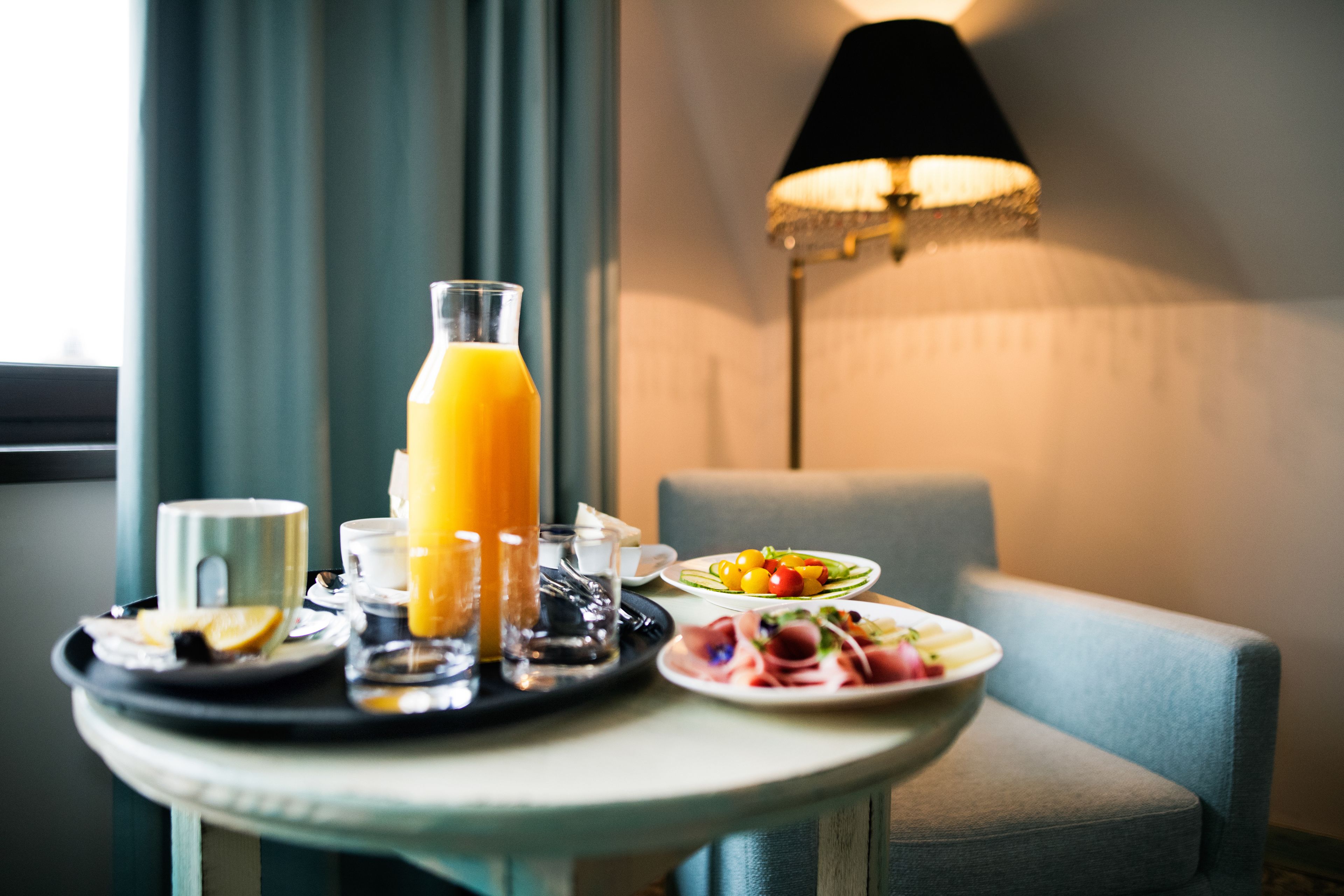 Een ontbijttafel met sinaasappelsap, een kop en een bord eten in een kamer met een lamp en een stoel.