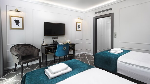 A hotel room with two beds, a desk, a chair, a television, and a door. - Hotel Golden Key 4 Stars Superior (Nitra)