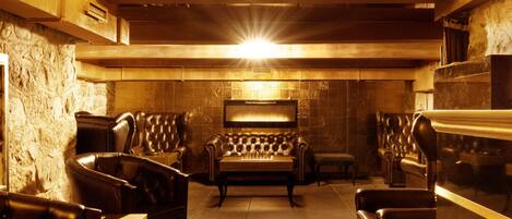 Una habitación con luz cálida, sofás de cuero, una mesa de centro de madera y una pared de piedra.