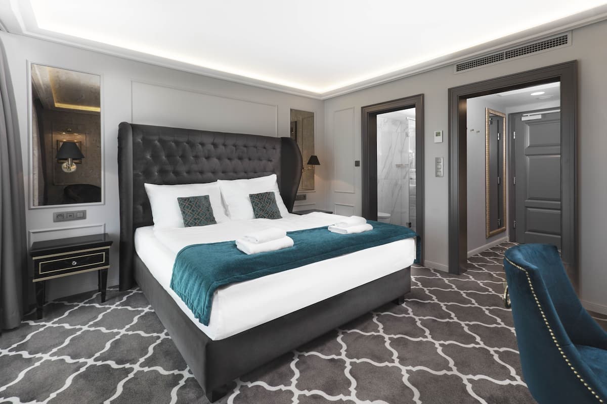 Une chambre d’hôtel moderne avec un grand lit, une table de chevet, un miroir et un fauteuil bleu.