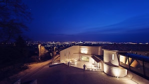 Un bâtiment à l’architecture incurvée, doté d’une entrée pavée et offrant une vue sur le paysage urbain illuminé la nuit.