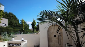 Un espace de douche extérieur moderne, agrémenté d’un mur en pierre, d’un palmier et d’un banc blanc avec des coussins.