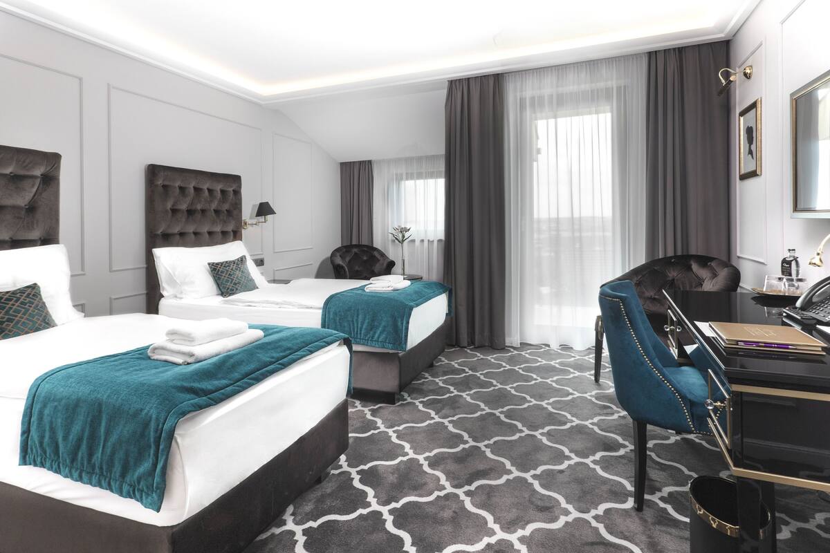 Une chambre d’hôtel avec deux lits, un bureau, une chaise et une grande fenêtre avec des rideaux.