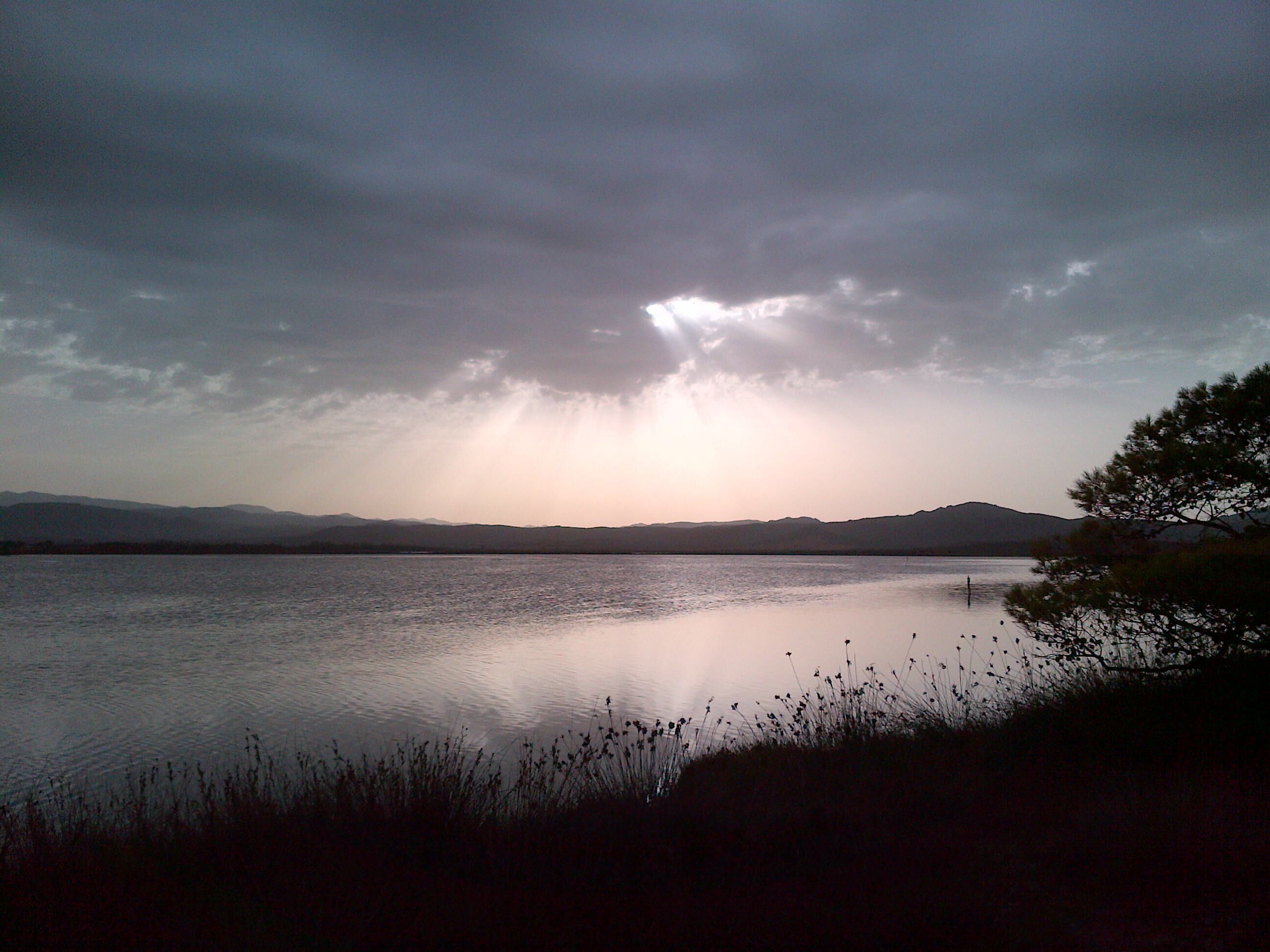Un lago tranquilo con montañas a lo lejos y un cielo nublado.