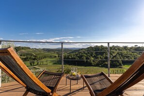 A terrace with two wooden lounge chairs and a table with glasses and a small bowl, overlooking a vineyard and hills. - Villa in Chianti with private pool, walking to a restaurant Electric car charger (Ortimino)