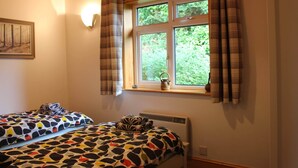 A bedroom with two beds, a window with curtains, a painting on the wall, and a radiator. - Delightful Detached Cottage close to Exeter, Dartmoor and the coast. (Longdown)