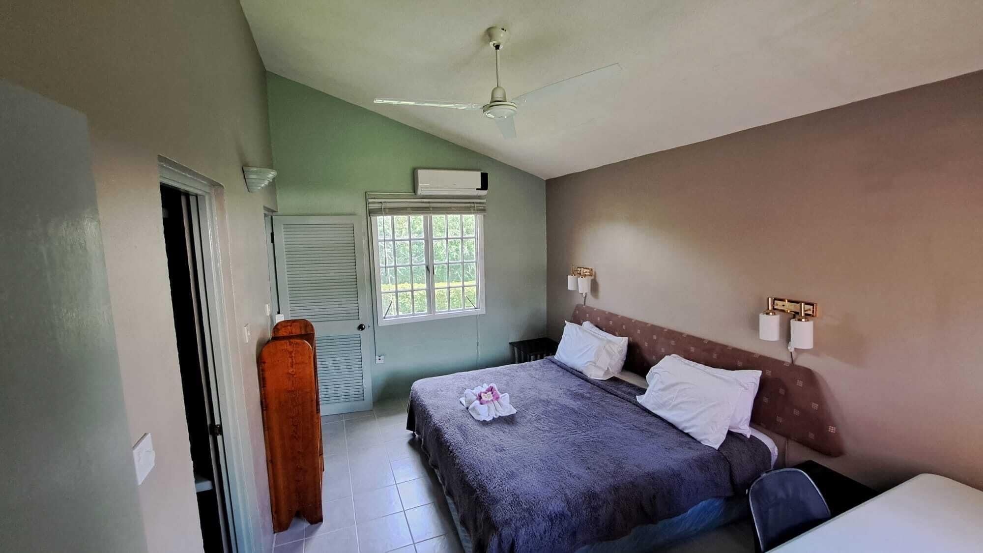 A bedroom with a bed, a window, an air conditioning unit, and a ceiling fan.