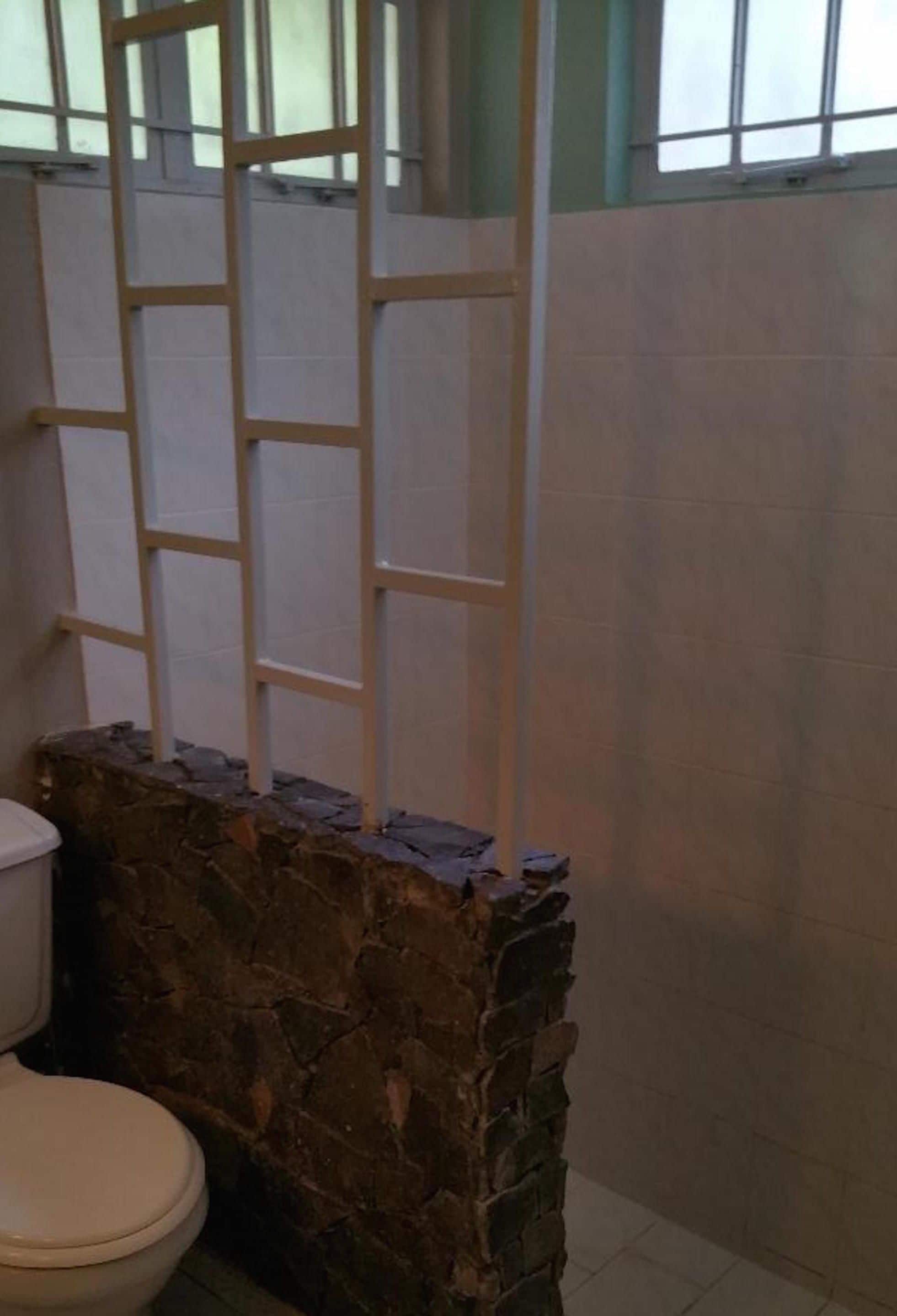 A bathroom with a stone wall, a toilet, and a window with bars.