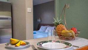 Una mesa de desayuno con un bol de frutas que contiene trozos de piña, manzana y mango, un vaso de agua, y un plato con tenedor y cuchillo.
