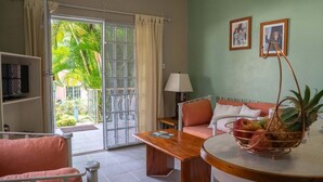 Una habitación con sofá, mesa, lámpara, televisor y ventana con vistas a palmeras.