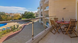 Ein Balkon mit Blick auf einen Pool, einem Esstisch mit Stühlen und blauem Himmel.