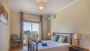 Ein Schlafzimmer mit Bett, Nachttischen, einem Sessel und einem Balkon, sowie einer Klimaanlage.