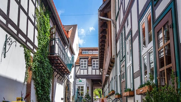 Eine enge Kopfsteinpflasterstraße mit traditionellen Fachwerkhäusern, einem Tisch mit Stühlen und Topfpflanzen.