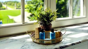 Una ventana con vistas a la vegetación, una planta en maceta y una bandeja con botellas.