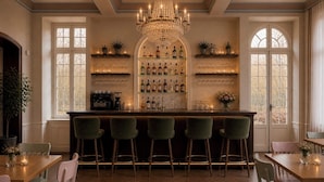 Zona de bar con candelabro, estanterías llenas de botellas y taburetes.
