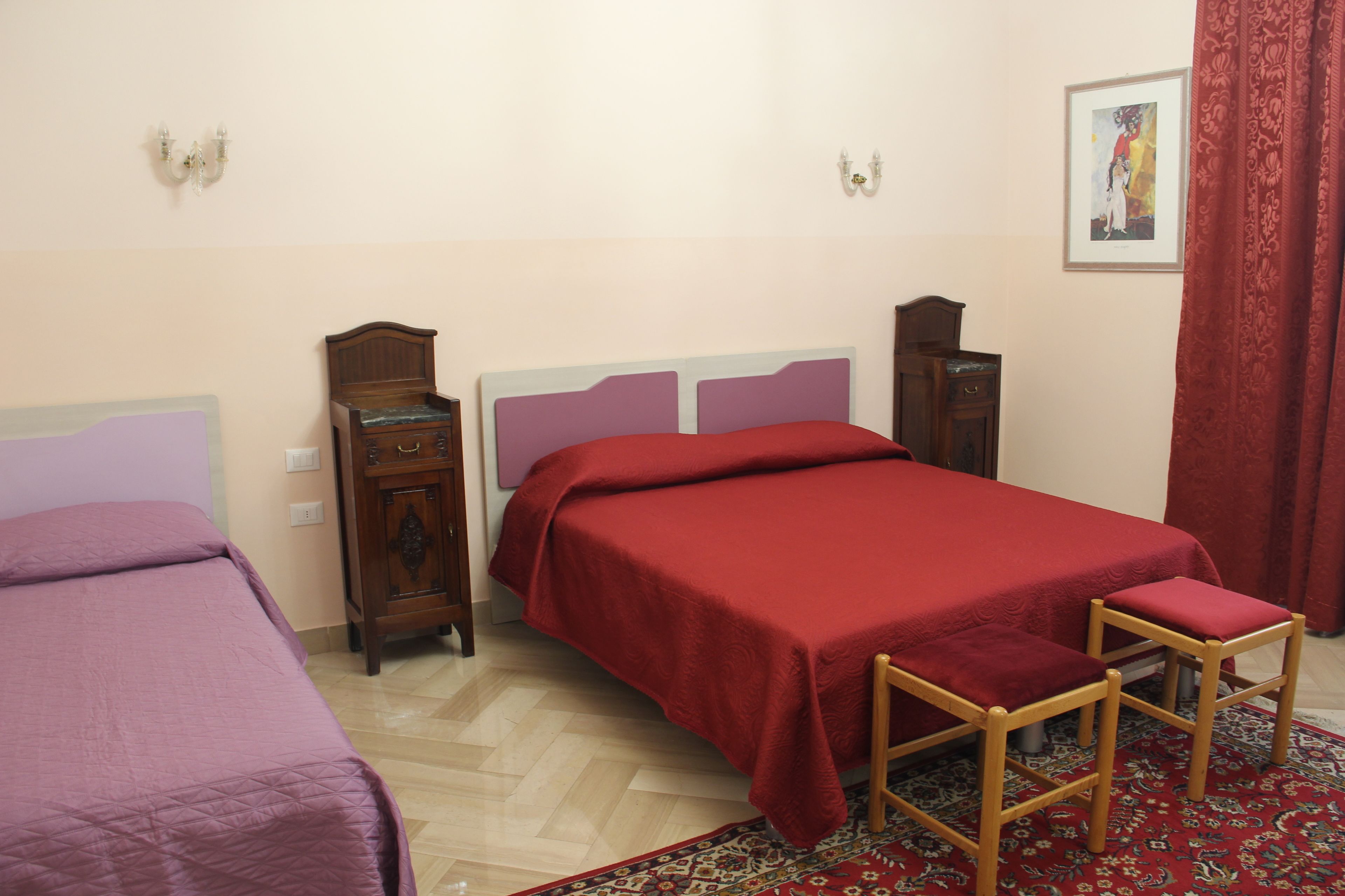 A bedroom with two beds, a wooden dresser, a nightstand, and a red curtain.