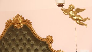 Un lit doté d’une tête de lit capitonnée et d’un ange doré tenant une lampe.