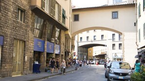Une rue bordée d’immeubles, avec une arche et des passants.