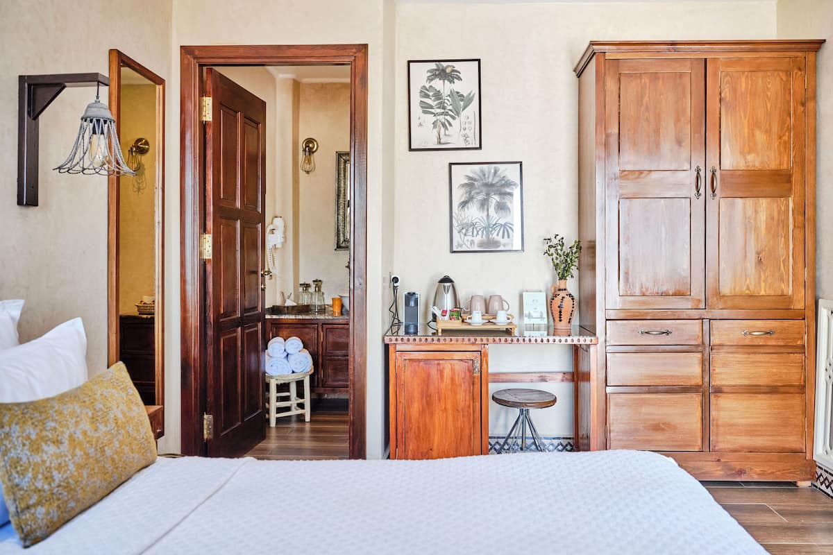 A bedroom with a bed, wooden wardrobe, and a small kitchenette.