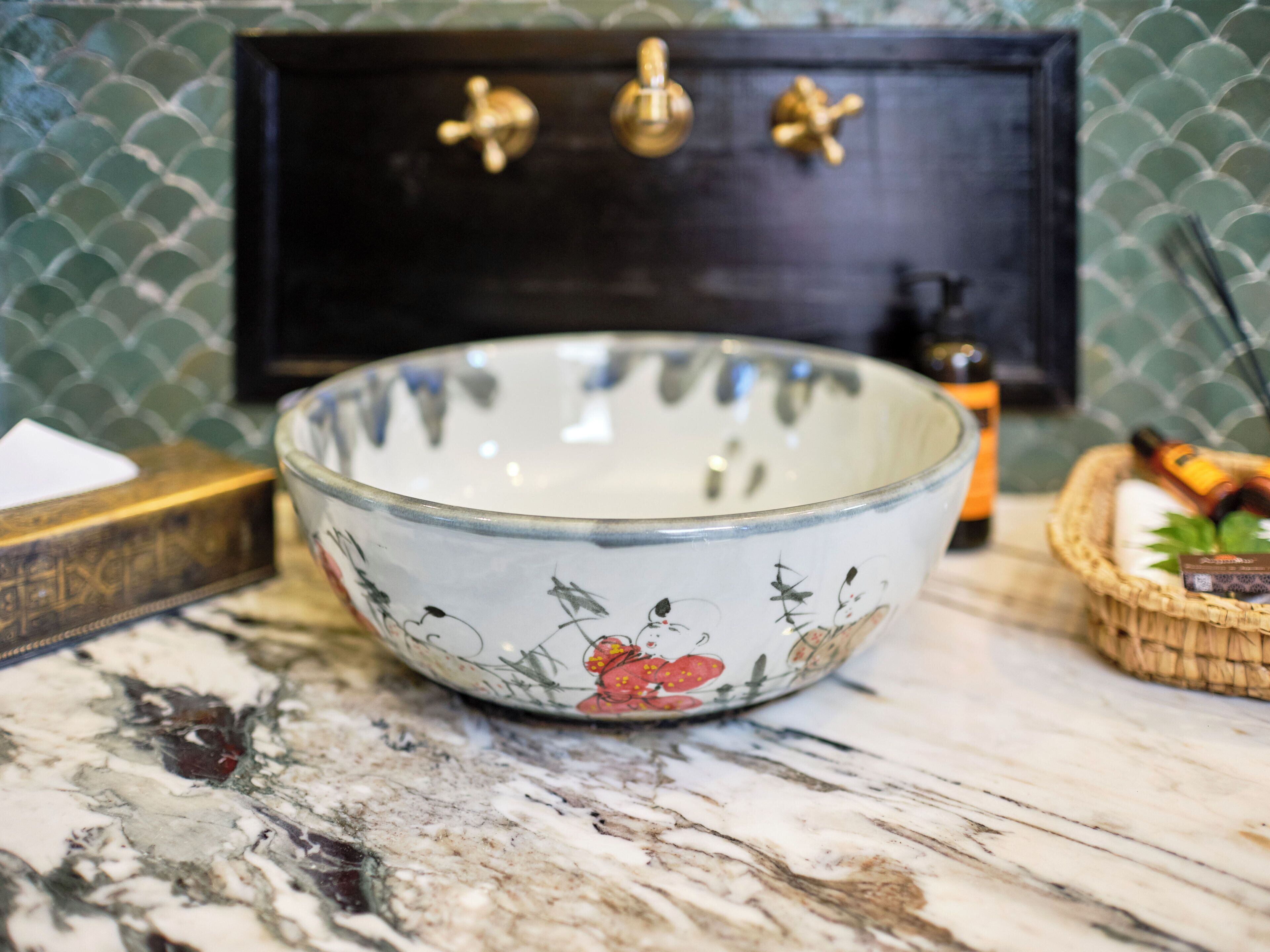 A bowl with floral patterns on a marble surface, a wooden box, and a small basket with items.