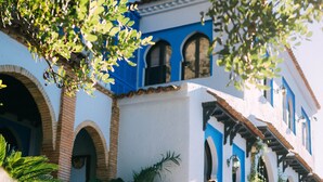 Una mujer con vestido blanco de pie frente a un edificio con paredes y arcos azules y blancos.