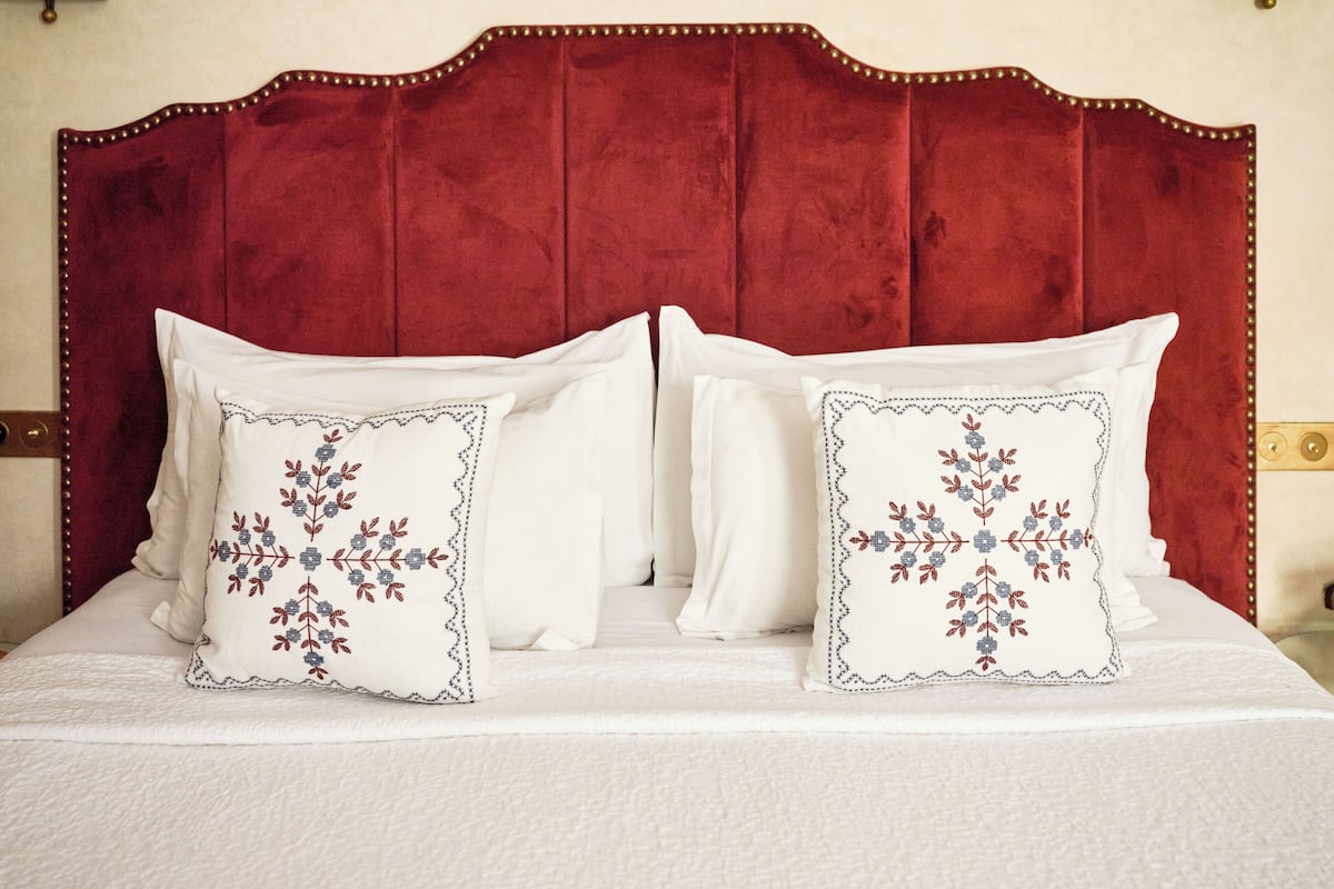 A bed with a red upholstered headboard, two white pillows with embroidered floral designs, and a white bedspread.