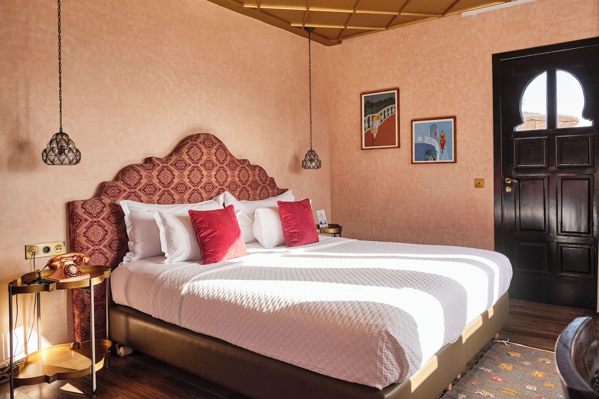 A neatly made bed with a patterned headboard, a bedside table with a telephone, and a door with a decorative handle.