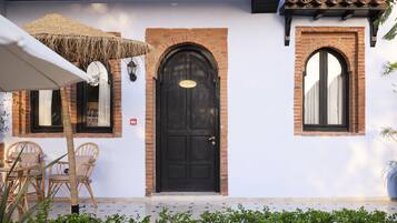Um edifício com porta preta, duas janelas e um pátio com piso cerâmico e móveis de vime.
